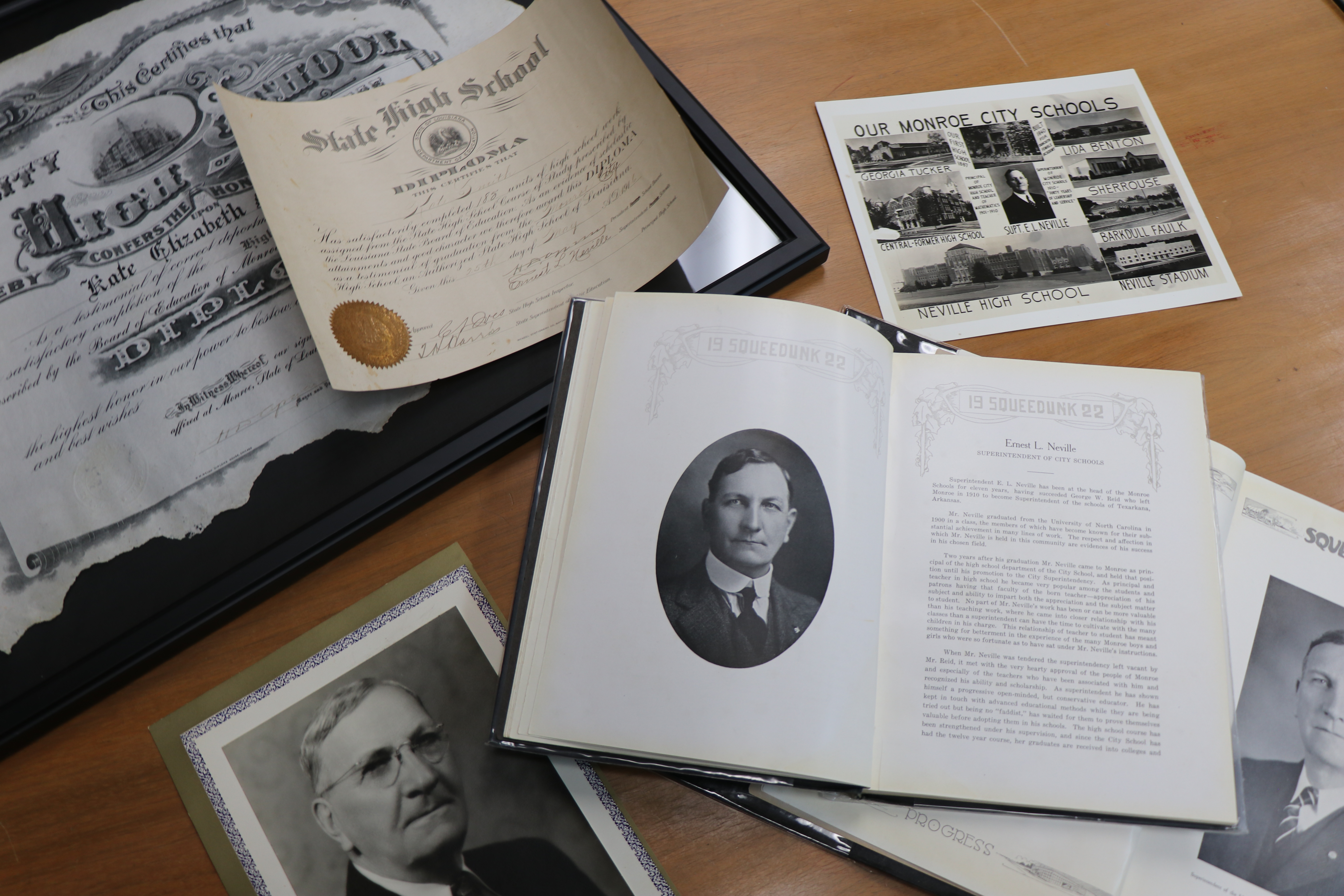 A table featuring various historical items: a portrait of Ernest Long Neville, a high school diploma, the Squeedunk 1922 yearbook open to a portrait of Ernest Neville