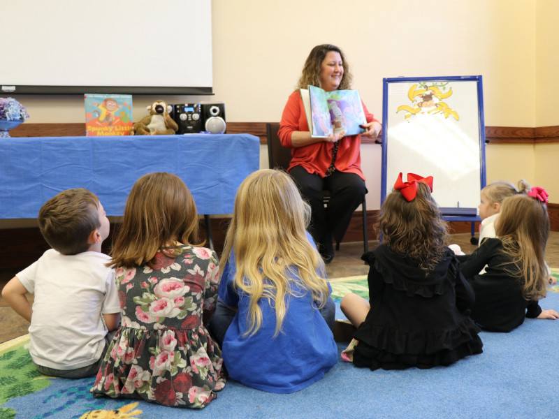 A librarian reads a story to a group of young children who are sitting on the floor around her.